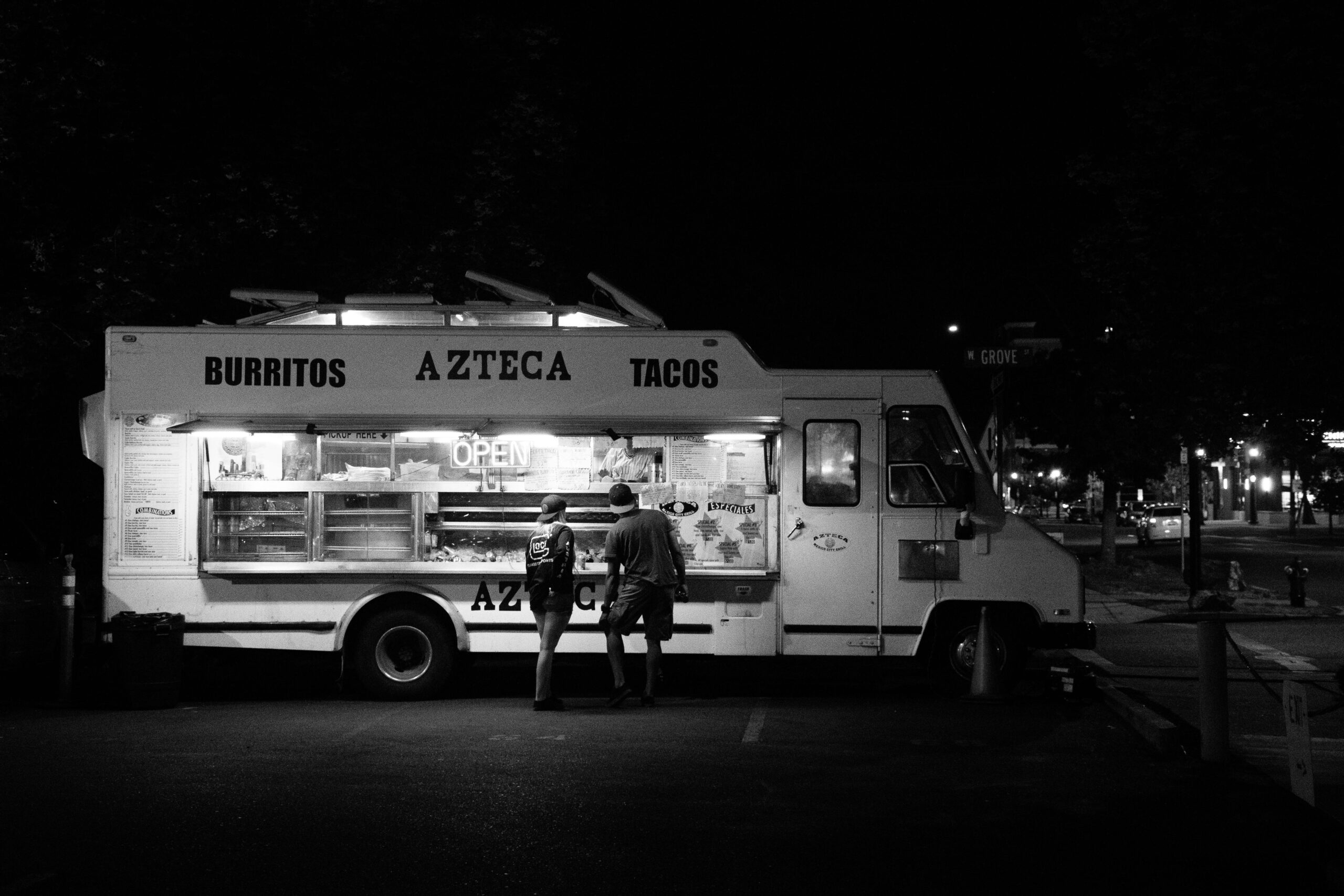 Black and white photo of people buying from a taco food truck at night.