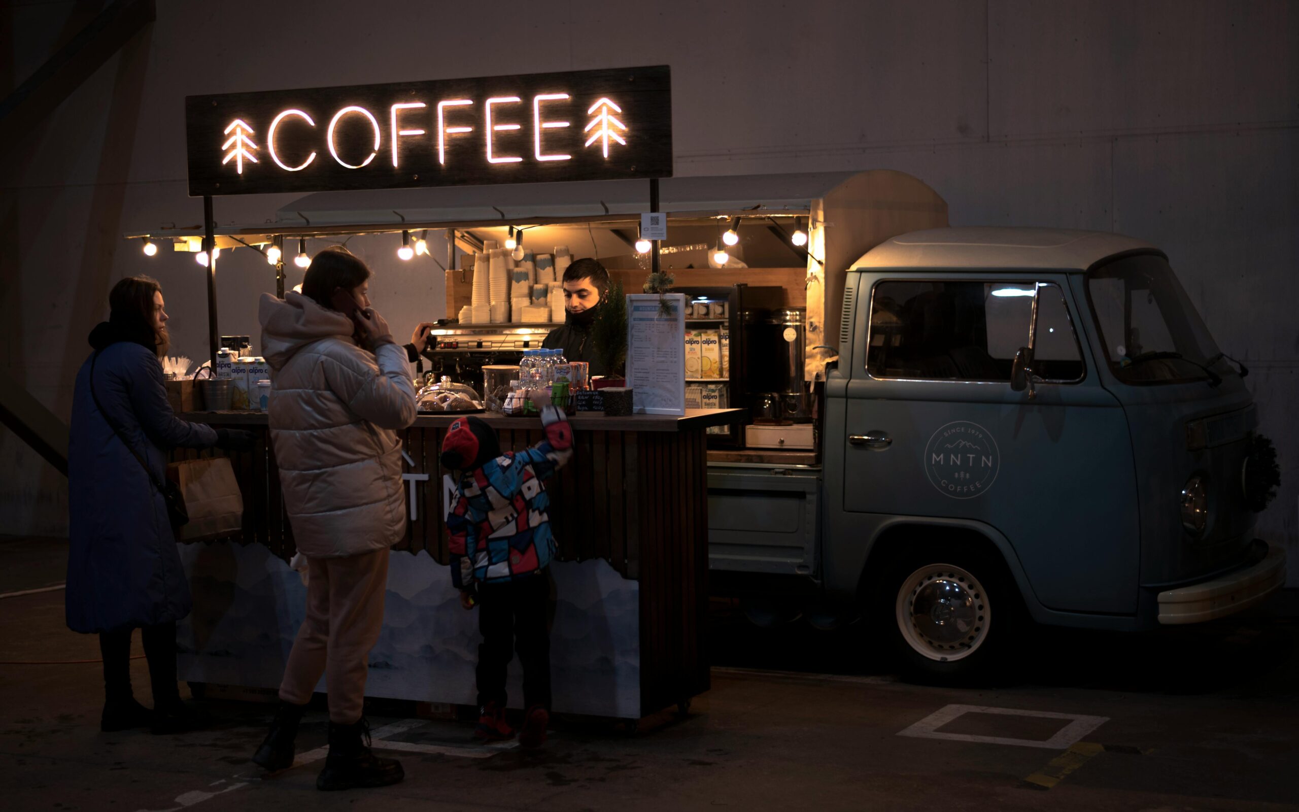 People gathered at a cozy nighttime coffee truck in an urban setting.